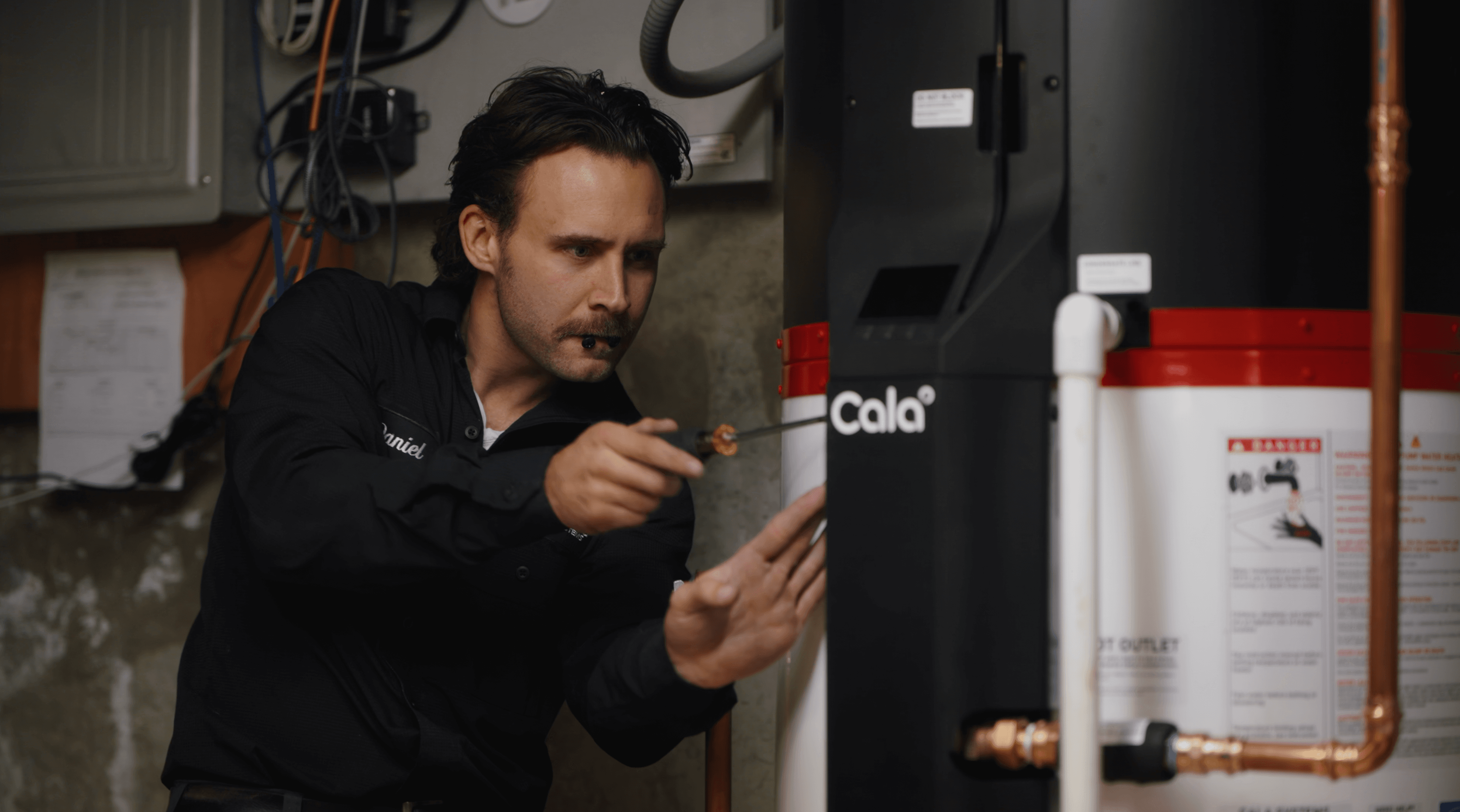 A SumZero technician making final checks on a newly installed Cala heat pump water heater in a basement.